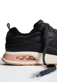 Sneaker nera in pelle con suola centrale di un leggero color beige e ammortizzazione d'aria trasparente. Presenta lacci testurizzati a contrasto e un design elegante.