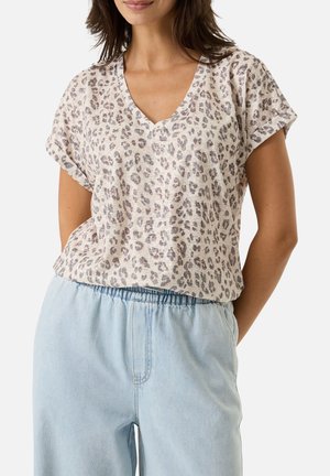Femme portant un haut beige à manches courtes avec col en V imprimé léopard, rentré dans un jean bleu clair à taille élastique.