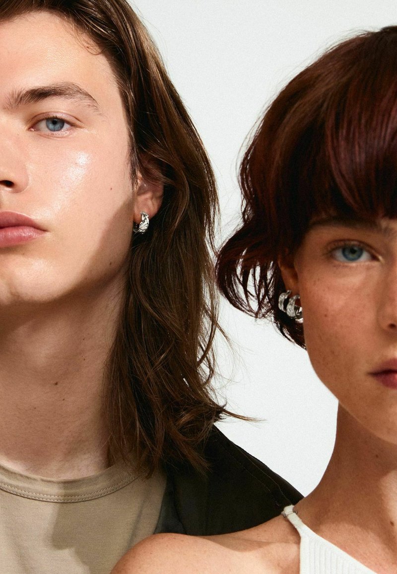 Due persone sono mostrate, indossando orecchini metallici. Una ha lunghi capelli castani; l'altra ha i capelli corti e scuri. Entrambi indossano abbigliamento neutro.