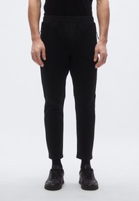 Czarne zwężane spodnie dresowe z elastycznym paskiem w talii, bocznymi kieszeniami i gładką fakturą. Połączone z czarnymi trampkami dla kontrastu.