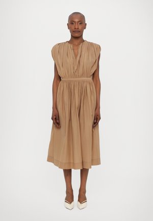 Robe plissée beige à coupe décontractée, taille froncée et manches courtes. Associée à des escarpins blancs à bout pointu, texture de tissu lisse.