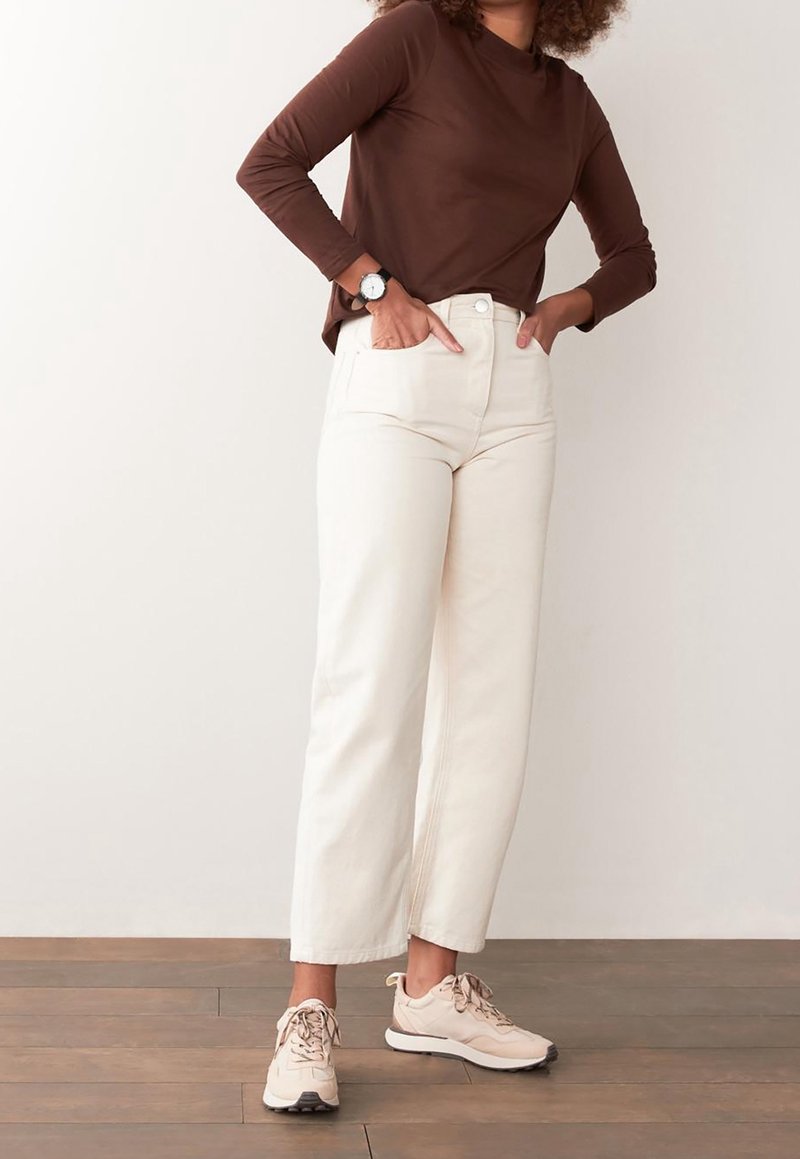 Brown long-sleeve top, cream wide-leg pants, and light beige sneakers. Features include a round neckline and two front pockets on the pants.