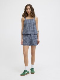 Débardeur bleu et blanc à motifs vichy avec décolleté carré, assorti à un short. Le modèle porte des baskets vertes et des chaussettes blanches.