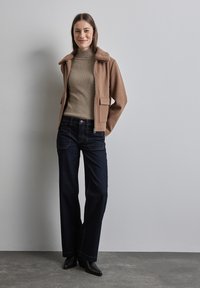 Braune Wollmischung Jacke mit einem Kunstfellkragen, kombiniert mit einem gerippten beige Rollkragenpullover und dunkelbblauen weit geschnittenen Jeans. Schwarze Stiefeletten mit Absatz.