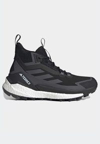 Chaussure de randonnée Adidas Terrex noire avec semelle blanche rembourrée et semelle extérieure robuste, tige en mesh et languettes sur la languette et le talon.