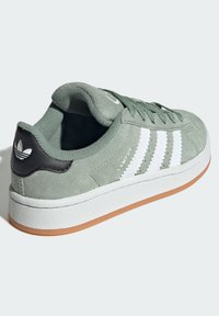 Zelené semišové tenisky s bielym trojpruhovým dizajnom, čiernym pätkovým pásikom a gumovou podrážkou. Obsahujú šnurovací systém a polstrovaný golier.