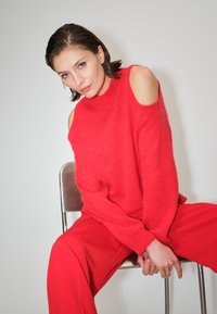 Rode gebreide trui met cold shoulder-design en een losse pasvorm, gecombineerd met rode wijde broek. Zachte textuur, eenvoudige halslijn en een ontspannen silhouet.