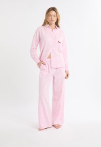 Set di pigiama in flanella rosa composto da camicia con bottoni e taschino sul petto decorato con ricamo di un bassotto, abbinato a pantaloni larghi con vita elasticizzata.