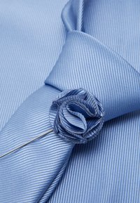 Light blue striped tie featuring a textured fabric and a fabric rose accent secured with a silver pin. Close-up perspective.