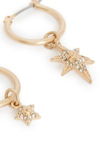 Guldtonade hoopörhängen med stjärnformade berlocker prydda med klara rhinestones, som visar en texturerad yta och intrikata detaljer.