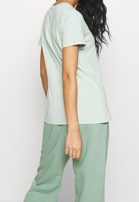 Ljusgrön bomulls-tshirt med korta ärmar, rund halsringning och avslappnad passform, tillsammans med matchande ljusgröna byxor. Slät textur.