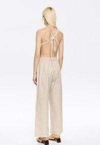 Beige backless top with thin straps, tied at the back, paired with loose beige trousers featuring an elastic waistband and wide legs.