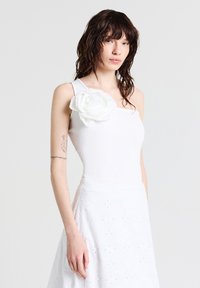 Top a righe bianco con una spalla sola, decorato con un grande fiore di tessuto bianco, abbinato a una gonna bianca ricamata.