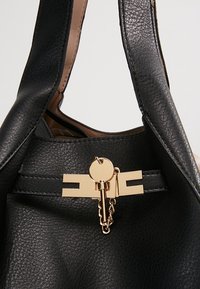 Musta nahkainen käsilaukku, jossa on sileä pinta, varustettu kultaisella kiinnityksellä ja ketjuyksityiskohdalla edessä. Hihnat ovat myös nahkaa.