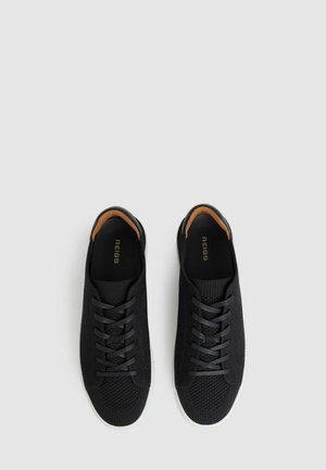 Schwarze Strick-Sneaker mit einem Mesh-Textur, runder Zehenpartie und kontrastierender weißer Gummisohle. Verfügt über eine Schnürung vorne und ein weiches Innenfutter.