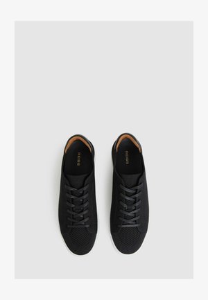 Schwarze Strick-Sneaker mit einem Mesh-Textur, runder Zehenpartie und kontrastierender weißer Gummisohle. Verfügt über eine Schnürung vorne und ein weiches Innenfutter.