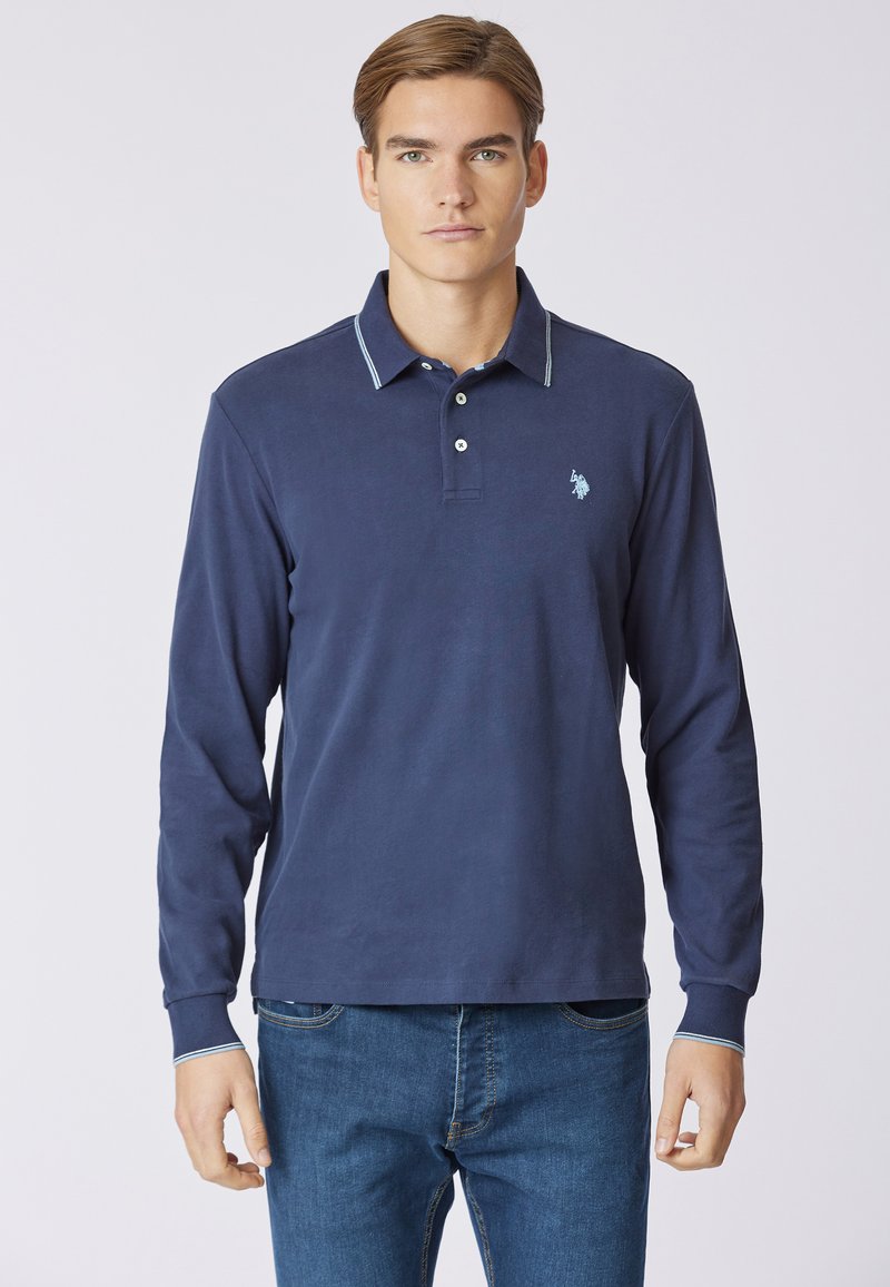 Polo a maniche lunghe di colore blu navy con colletto classico, caratterizzato da un accento azzurro chiaro lungo il bordo del colletto e un piccolo logo sul lato sinistro del petto.