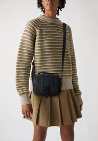 Black leather crossbody bag with a textured finish, rectangular shape, and a front strap closure. Worn with a striped sweater and pleated skirt.