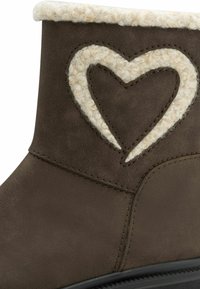 Hnědé semišové kotníkové boty s bílým umělým kožíškem na okraji a vyšitým designem srdce. Gumová podešev se symetrickým šitím.
