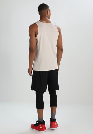 Canottiera beige chiaro da uomo, pantaloni corti neri, leggings neri e scarpe da ginnastica rosse. La canottiera presenta un design semplice senza motivi.
