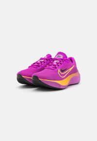 Růžové a žluté běžecké boty Nike s texturovaným síťovaným svrškem, šněrováním a černou gumovou podešví. Elegantní design s nízkým profilem.