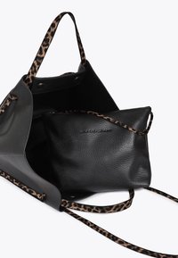 A black tote bag with leopard print straps, featuring a smaller black pouch inside. The interior is spacious and unadorned.