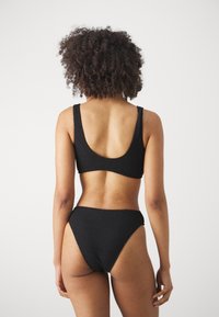 Čierny bikiny set s textúrovanou, rebrovanou tkaninou. Vrchný diel má široké ramienka a nízky chrbát, zatiaľ čo spodné diely majú strih s vysokým vykrojením.