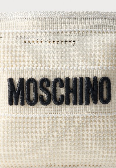 Gros plan sur un tissu texturé couleur crème avec des lettres noires, épaisses et enroulées de fil formant le mot « MOSCHINO » au centre.