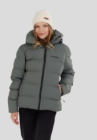 Puffer takki oliivinvihreänä, jossa on vetoketjukiinnitys, kiristettävä huppu ja mustat yksityiskohdat, yhdistettynä vaalean kermanväriseen neulottuun myssyyn.