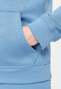 Light blue sweatshirt with a front pocket and ribbed cuffs. Soft cotton material features a textured finish and stitched detailing.