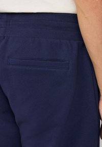 Navy blauwe joggingsbroek met een gladde katoenen textuur, voorzien van een enkele achterzak en een elastische tailleband voor comfort.