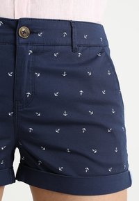 Námořnické šortky vyrobené z bavlny, s vzorem malých bílých kotviček. Lem je ohrnutý a v pase je zapínání na knoflík.