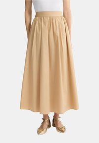 Gonna beige lunghezza ginocchio con vita arricciata, realizzata in tessuto liscio. Abbinata a ballerine dorate con cinturini incrociati.