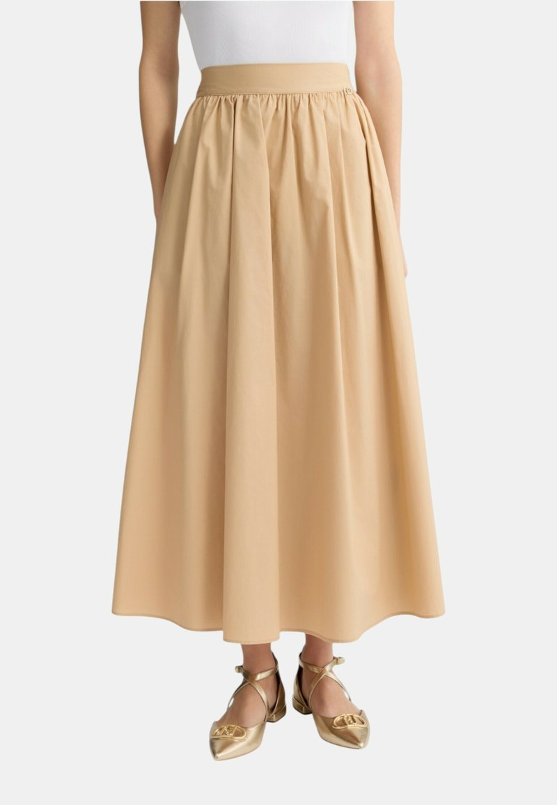 Gonna beige lunghezza ginocchio con vita arricciata, realizzata in tessuto liscio. Abbinata a ballerine dorate con cinturini incrociati.