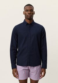 Μπλε ναυτικό πουκάμισο με κουμπιά, μακρυμάνικο, από βαμβάκι, με γιακά και εμπρόσθια πατιλέτα. Φορεμένο με ροζ ριγέ σορτς.