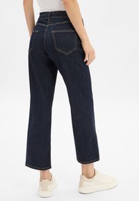 Jeans droits bleu marine avec poches arrière visibles et coutures contrastées. Associés à des baskets blanches, photographiés de l'arrière.