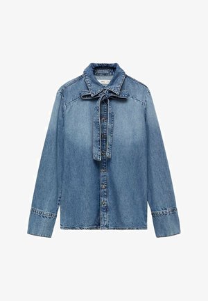 Svijetloplava traper košulja dugih rukava, s dugim kopčanjem sprijeda i mašnom vezanom oko ovratnika. Ima klasičnu traper teksturu i šavove.