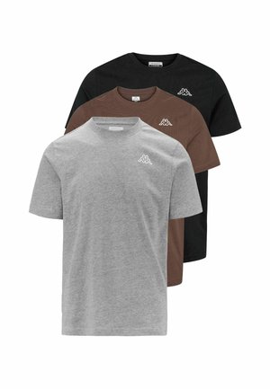 Homme portant un t-shirt gris uni à manches courtes avec un petit logo sur la poitrine, associé à un jean bleu, debout devant un fond blanc.