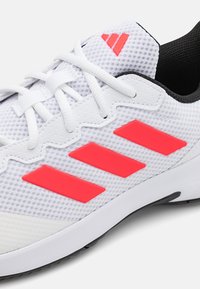 Chaussure de sport blanche avec tige en mesh, doublure noire et accents roses. Présente trois rayures roses sur le côté et des lacets plats.