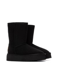 Bottes en daim noires mi-mollet avec une semelle en caoutchouc plate, présentant une texture lisse, un design épuré et un détail de marque à l'arrière.