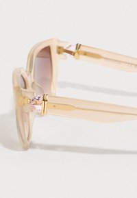 Transparente solbriller med lys rosa gradientlinser, dekorative krystallakkenter og hardware i gulltone på bøylene.