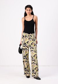 Wide-leg trousers featuring a colorful tropical leaf print in green, black, and beige. Made from lightweight fabric with an elastic waistband.