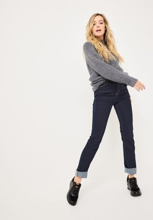 Gray ribbed sweater with long sleeves, paired with dark jeans featuring rolled cuffs and black lace-up sneakers. Simple and modern design.