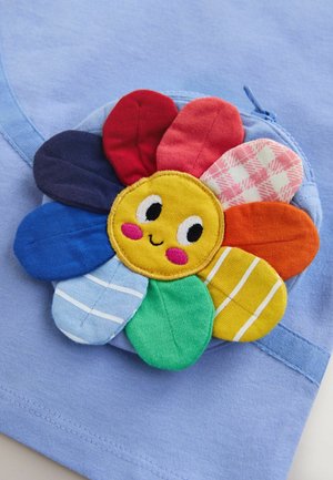 Jasnoniebieska tkanina z teksturowaną, wielokolorową aplikacją kwiatu składającą się z różnych materiałów, z uśmiechniętym żółtym środkiem i różnorodnymi wzorami płatków.