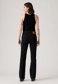 Zwarte mouwloze tanktop gecombineerd met hoog-waisted, rechte jeans. De jeans hebben klassieke achterkantzakken en een tan leren label op de tailleband.