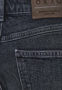 Ciemnoniebieskie dżinsy z teksturowanej tkaniny. Posiadają skórzaną metkę marki oraz kontrastowe przeszycia. Zawierają projekt tylnej kieszeni.