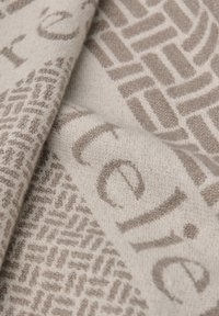 Beige stof med et tekstureret design af geometriske mønstre og trykte bogstaver. Blød, fyldig tekstur med kontrasterende lyse og mørke nuancer.