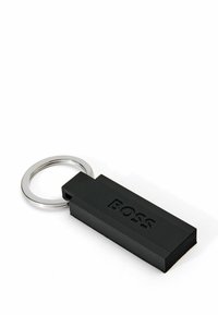 Zwarte rubberen sleutelhanger met een gestructureerd oppervlak, voorzien van een gegraveerd logo en een glanzende metalen ring voor bevestiging.