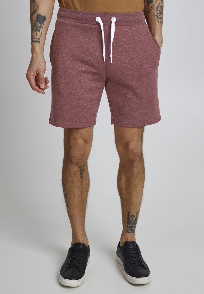 Pantalones cortos burdeos con cintura elástica, material de mezcla de algodón y bolsillos laterales. Combinados con zapatos negros. Textura suave y diseño hasta la rodilla.