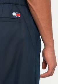 Sötétkék nylon rövidnadrág hátsó zsebbel. A Tommy Jeans logó vörös, fehér és kék hímzéssel van ellátva. Sima, könnyű textúra.